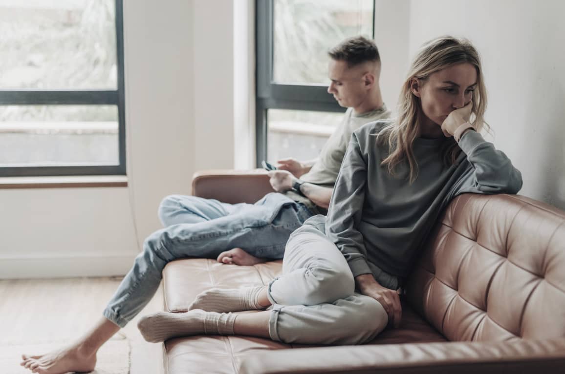 "Kvinna och man sitter tysta i soffan, vända från varandra – symbol för konflikträdsla och osagda ord i relationer."