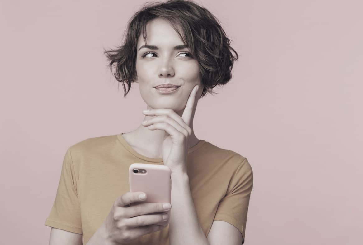 Kvinna håller i en mobil och ser fundersam ut – symboliserar skillnaden mellan önskan, gräns och ultimatum.