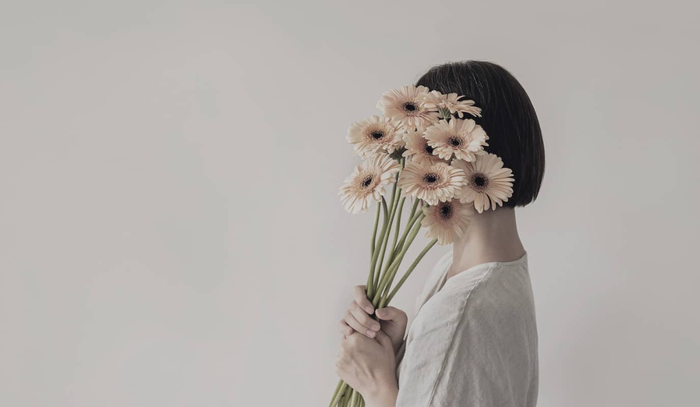 Person som gömmer ansiktet bakom en bukett blommor – symbol för medberoende och att tappa bort sig själv.