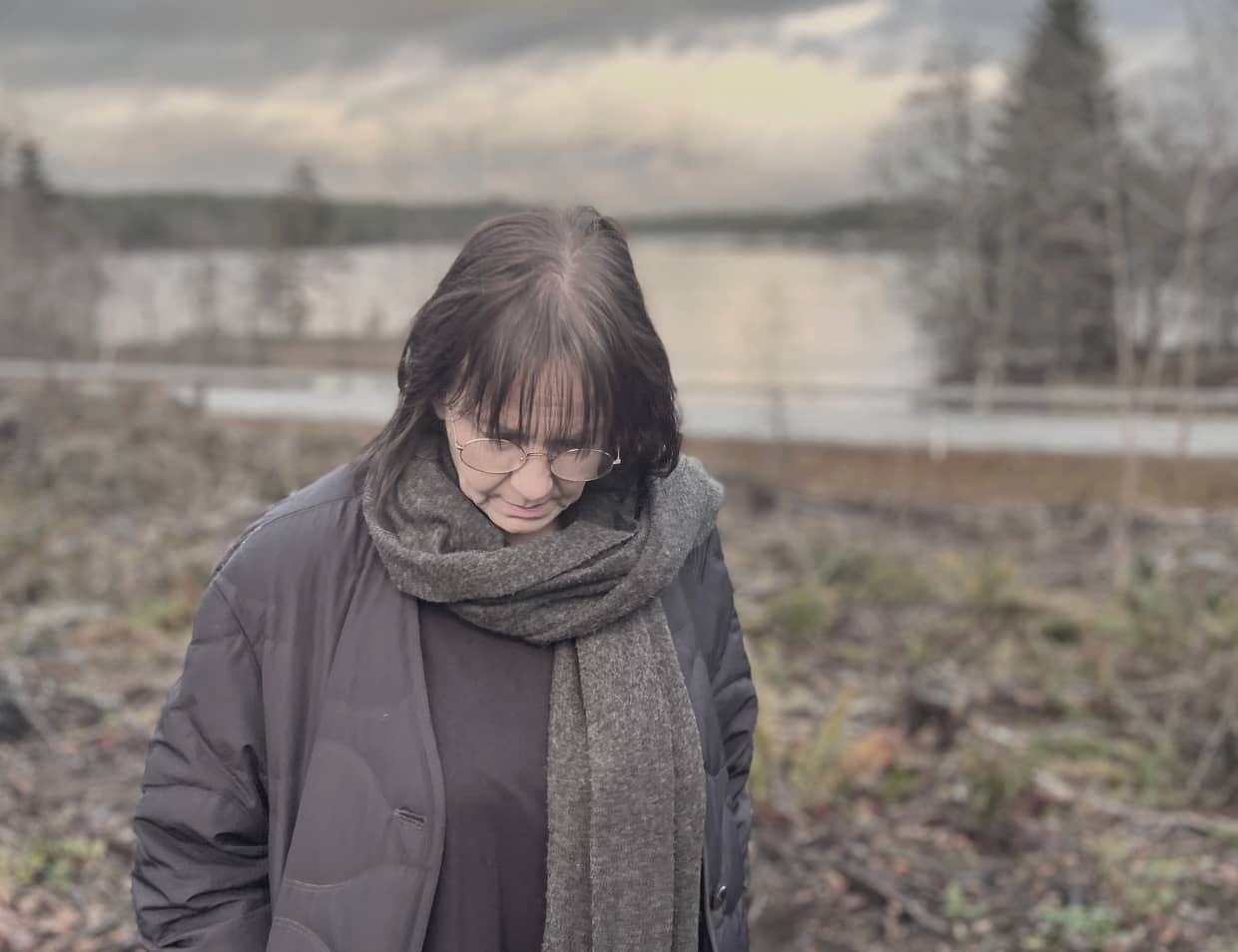 Kvinna står utomhus med blicken nedåt, omgiven av natur, en lugn och eftertänksam stund som speglar temat medberoende och kraschen.