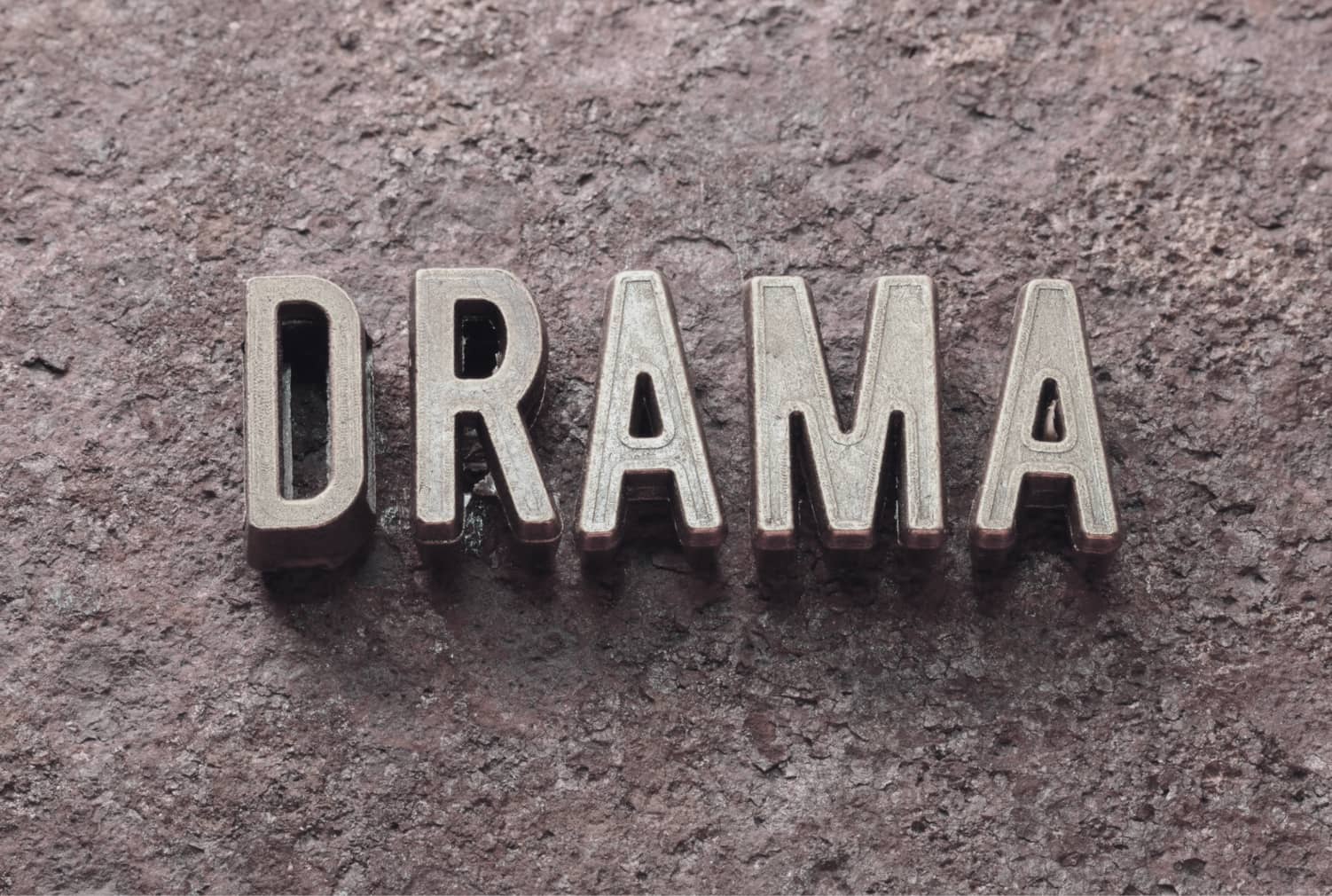 Metallbokstäver som bildar ordet “DRAMA” på en rå stenbakgrund, en visuell symbol för medberoende och dramatriangeln.
